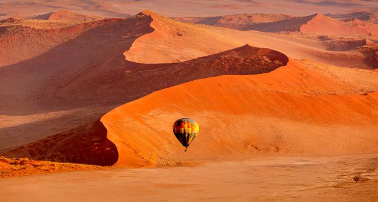 Un colorido globo aerostático flota sobre las imponentes dunas rojas del Desierto de Namibia.