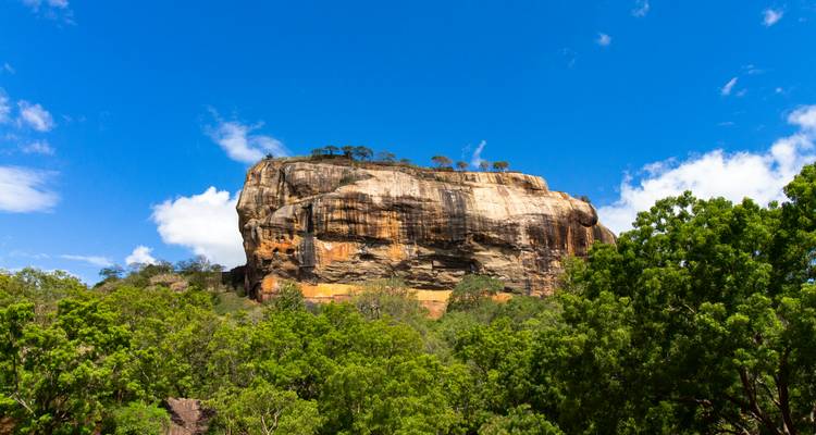 La cara de granito puro de la Roca de Sigiriya se eleva sobre la densa selva tropical bajo un cielo azul brillante.