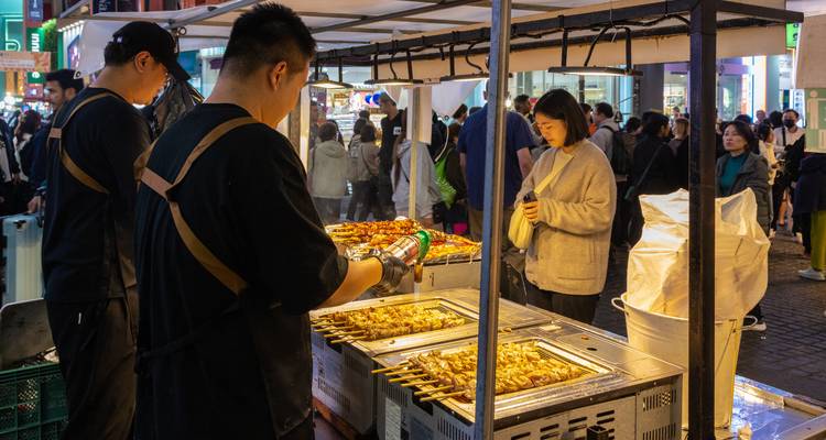 Vendeur de street food grillant des brochettes sur un marché nocturne animé