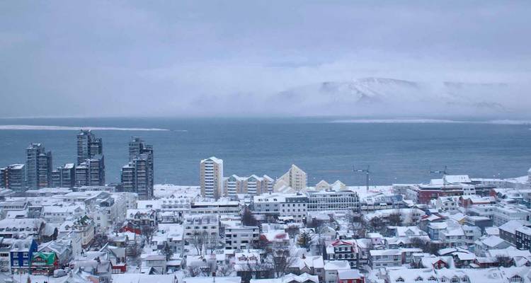 Skyline hivernale de Reykjavik couverte de neige avec l'océan et les montagnes brumeuses au-delà.