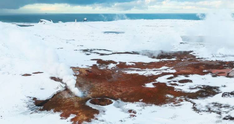 Vue aérienne d'un champ géothermique avec des évents fumants au milieu d'un paysage islandais couvert de neige.