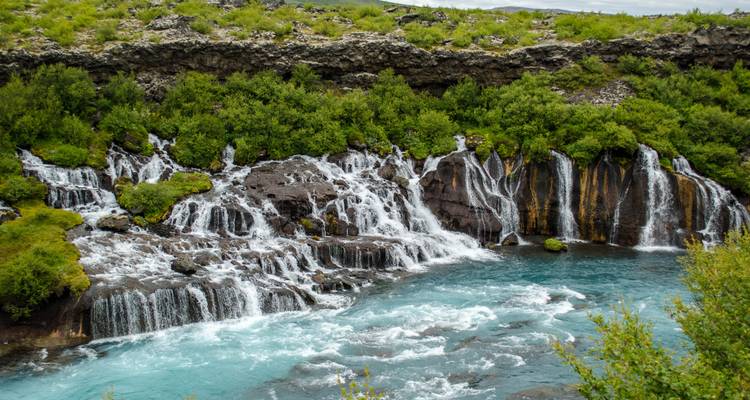 Een ander perspectief van Hraunfossar waar talloze stromen door lavarots in aquablauw water stromen.