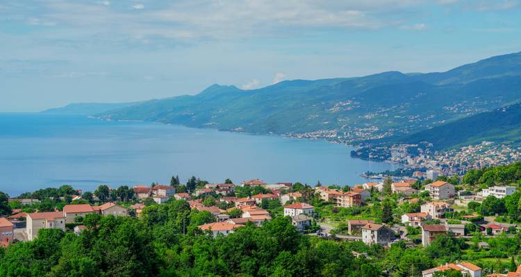 Weite Küstenpanorama mit Ziegeldachdörfern entlang einer tiefblauen Bucht der Adria, im Hintergrund von Hügeln begrenzt