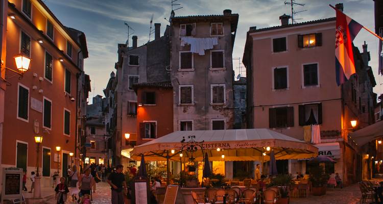 Abendliche Szene eines lebhaften Altstadtplatzes mit Cafés und warmer Straßenbeleuchtung