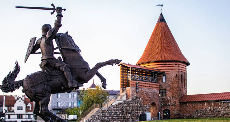 Reiterstatue mit gezücktem Schwert neben dem rotgedeckten Turm der Burg Kaunas