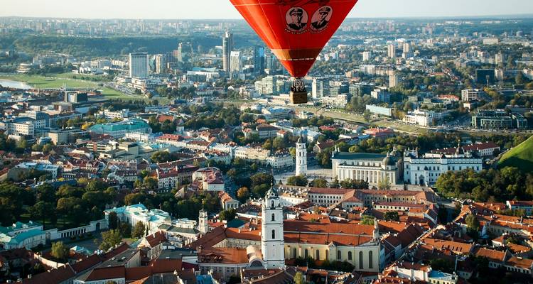 Rotglühender Heißluftballon, der über die historischen Dächer und grünen Parks von Vilnius schwebt