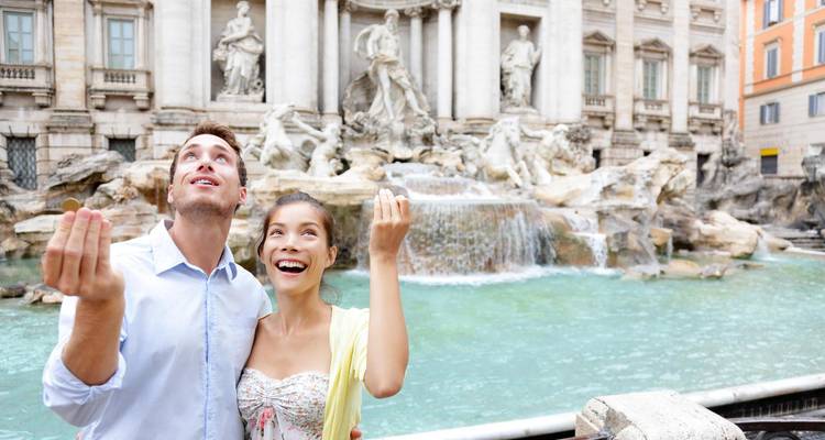 Un couple souriant jette des pièces de monnaie dans la fontaine Baroque ornée avec ses chutes d'eau en cascade et ses statues en marbre.