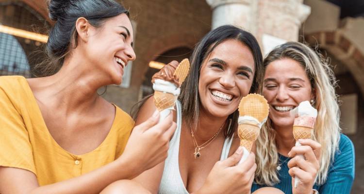 Trois amis joyeux dégustant des cônes de glace tout en riant ensemble à l'extérieur.