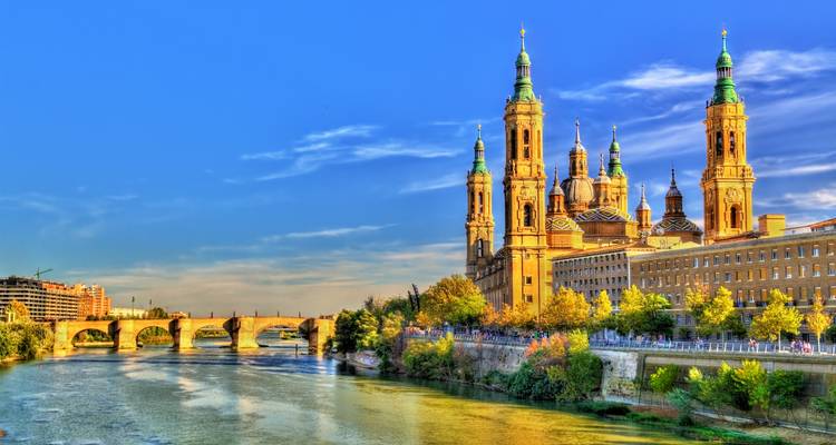 Vue vibrante de la Basilique de Nuestra Señora del Pilar dominant le fleuve Èbre et le pont de pierre historique dans une lumière chaleureuse.