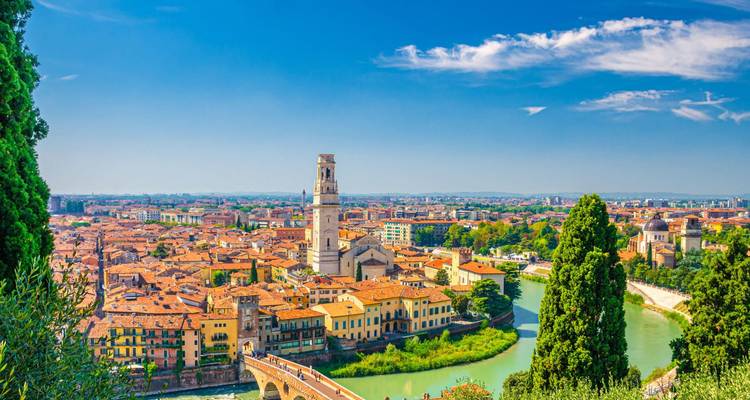 Vista panorámica brillante del centro histórico de Verona, el recodo del río y el campanario enmarcados por la vegetación y los cielos azules.