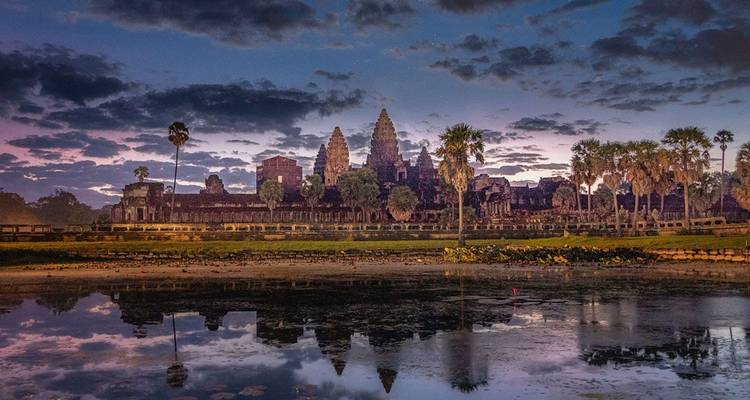 Los icónicos torres de Angkor Wat se recortan contra un cielo púrpura al amanecer, reflejándose perfectamente en un estanque de lotos inmóvil.