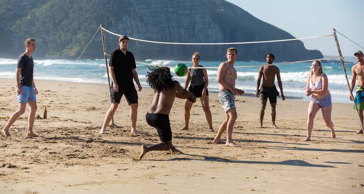Groupe énergique jouant au volley-ball de plage avec les vagues de l'océan et une falaise en arrière-plan