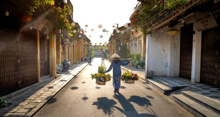 Mit Laternen gefüllte Straße von Hoi An mit einem einzelnen Verkäufer, der Blumentöpfe in ausbalancierten Körben trägt