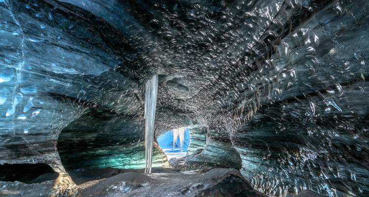 Una impresionante cueva de hielo glacial azul con paredes texturizadas brillantes y una apertura luminosa hacia el exterior.