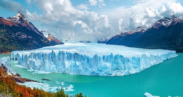 Immenser türkisfarbener See, begrenzt durch die aufragende eisige Wand des Perito-Moreno-Gletschers unter dramatischen Wolken.