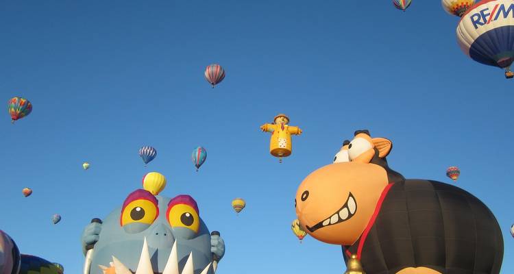 Ballonnen in grappige vormen stijgen op tegen een diepblauwe lucht tijdens een ballonfestival.