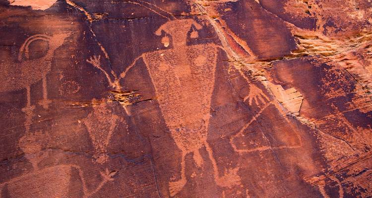 Oude rotstekeningen in roodachtig zandsten tonen menselijke en dierlijke figuren.