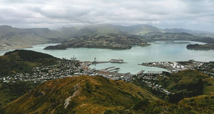 Une petite ville portuaire nichée autour d'une baie tranquille, vue depuis une crête élevée avec des collines ondulantes au-delà.