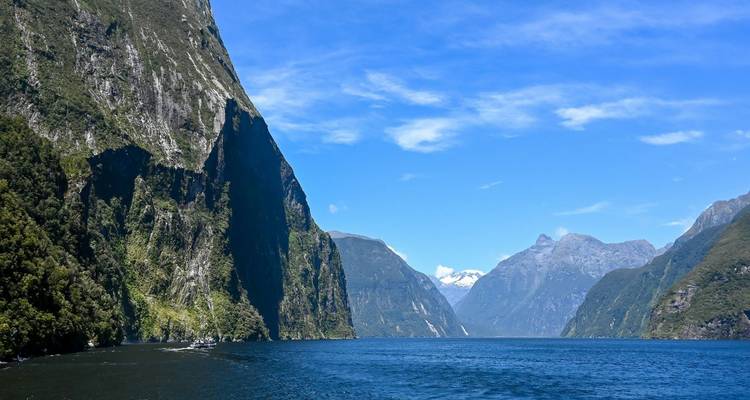 Acantilados empinados y boscosos se alzan desde las aguas azul profundo del Milford Sound en un día despejado.