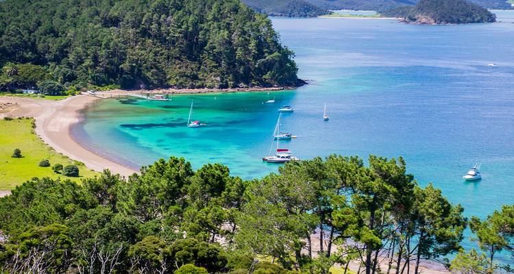 Bahía de un vibrante turquesa con veleros anclados cerca de frondosos acantilados verdes