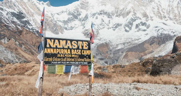 Cartel que dice 'Namaste Annapurna Base Camp' con el fondo de las nevadas cimas del Himalaya.