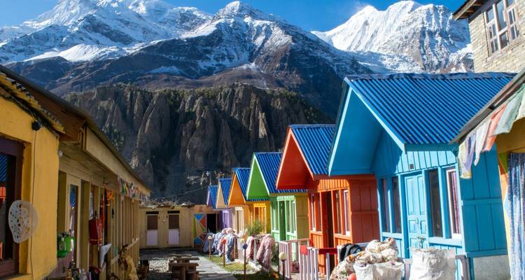 Fila de alojamientos pintados con colores brillantes bajo los acantilados del Annapurna que se alzan imponentes