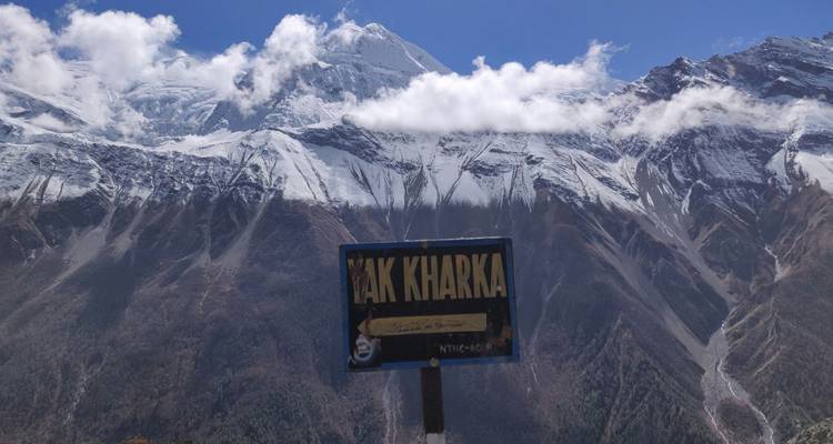 Cartel indicador de Yak Kharka con el telón de fondo de las montañas del Himalaya cubiertas de nieve bajo las nubes