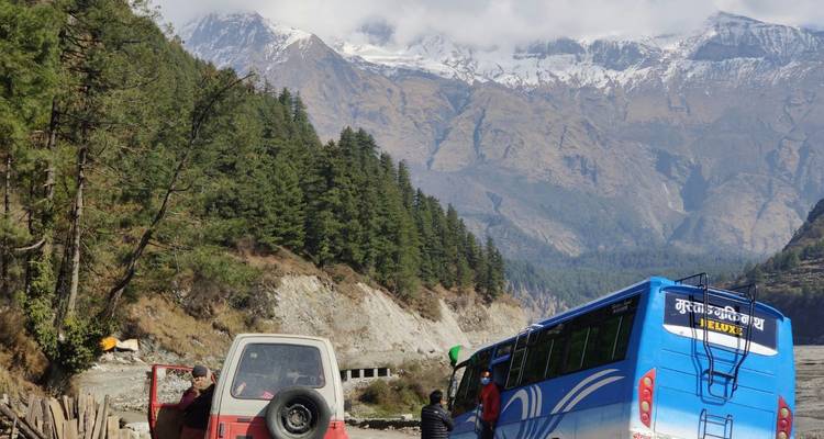 Viajeros de pie junto a un autobús en un camino de grava con el Himalaya brumoso de fondo