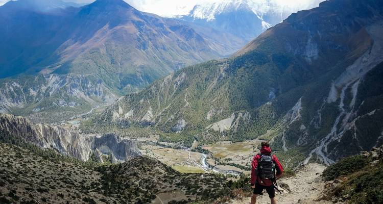 Trekker en solitario contemplando un amplio valle verde y río bajo picos imponentes
