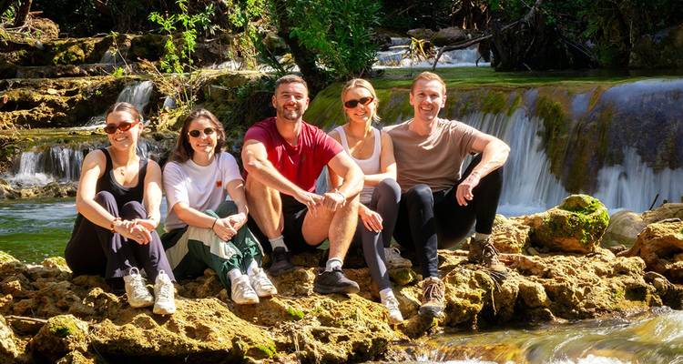 Groep wandelaars die rust nemen bij een kleine waterval met trappen in een weelderige bosomgeving