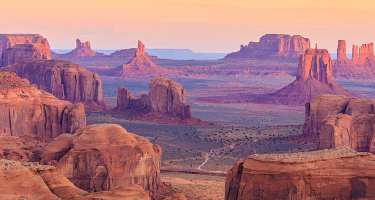 Icónicas mesetas y peñascos de arenisca roja que brillan al atardecer en un amplio valle desértico