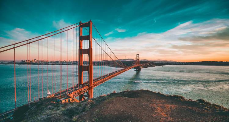 Le Golden Gate Bridge s'étend à travers la baie au lever du soleil avec des couleurs de ciel vibrantes et un bateau en dessous