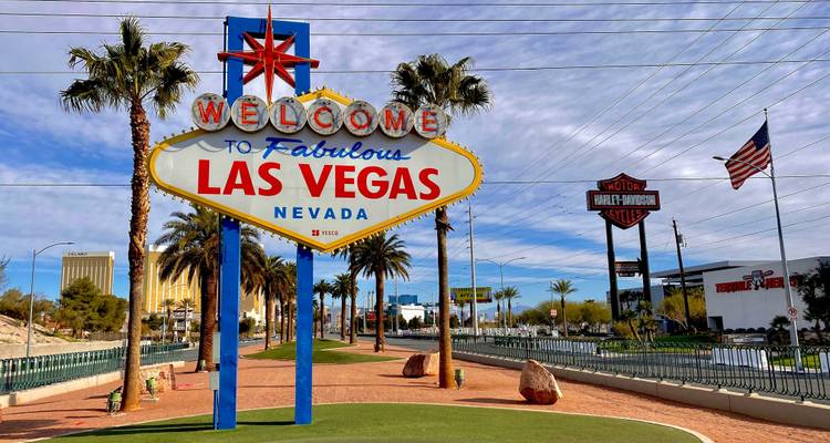 Vue diurne de l'emblématique panneau "Welcome to Fabulous Las Vegas" aux couleurs éclatantes sur un ciel partiellement nuageux.