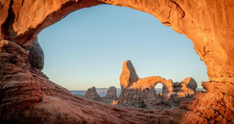 Los marcos de arenisca natural enmarcan torres y arcos lejanos en la luz dorada del amanecer en el Parque Nacional Arches.