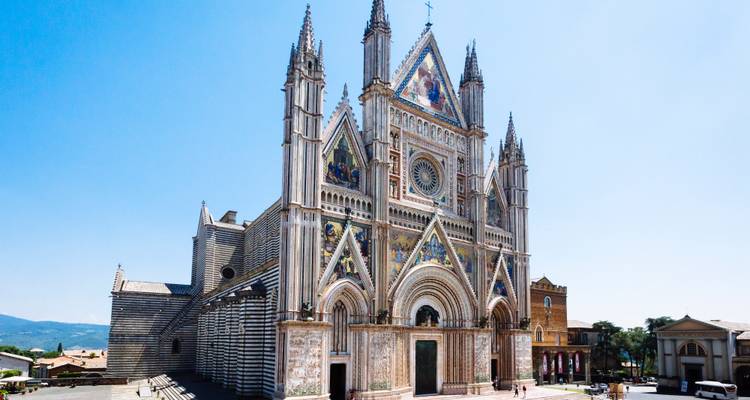 Prachtvolle Fassade der Kathedrale von Orvieto, geschmückt mit farbenfrohen Mosaiken und Rosettenfenster unter klarem Himmel.