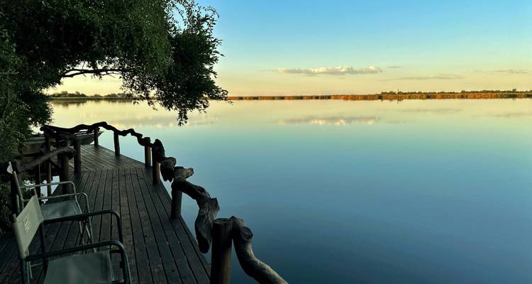 Peaceful wooden deck with chairs over still river reflecting soft pastel evening sky.