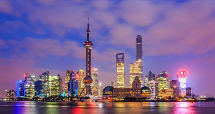 Illuminated Shanghai skyline with the Oriental Pearl Tower and modern skyscrapers reflecting on the Huangpu River after dusk.