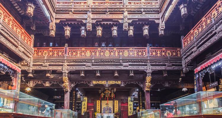 Ornate interior hall with carved wooden balconies, red and gold detailing, and a central shrine display.