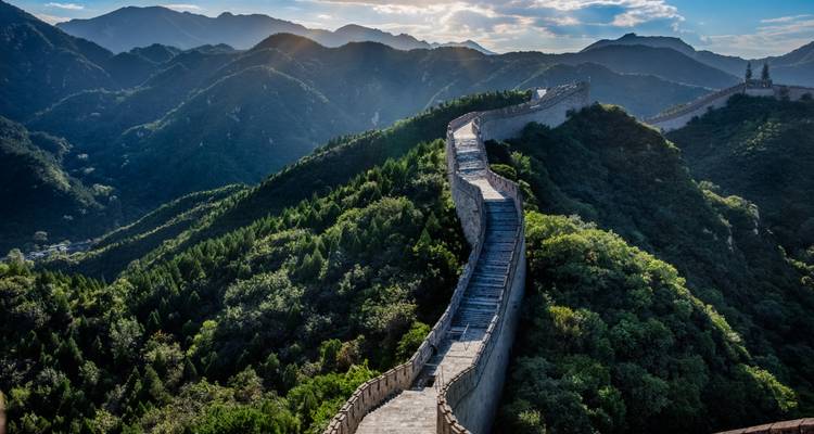 The Great Wall of China winding over lush green mountain ridges illuminated by low golden sunlight.
