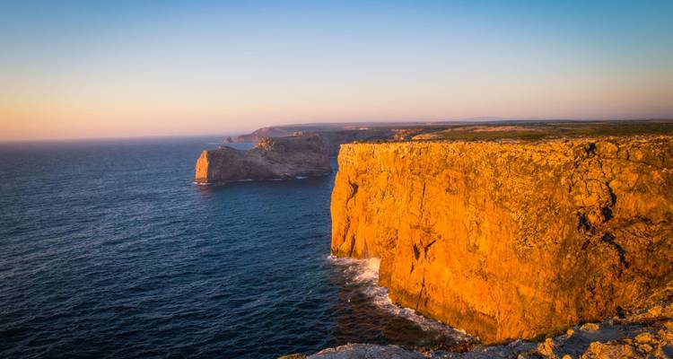 Des falaises marines spectaculaires d'orange éclatant à Sagres qui brillent à la lumière du coucher de soleil au-dessus des eaux bleu profond de l'Atlantique.