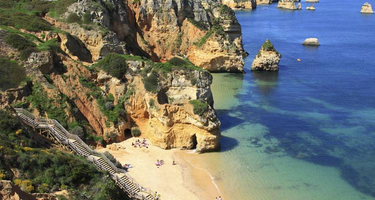 Cala turquesa con playa de arena ubicada entre acantilados espectaculares a la que se accede por una escalera de madera.
