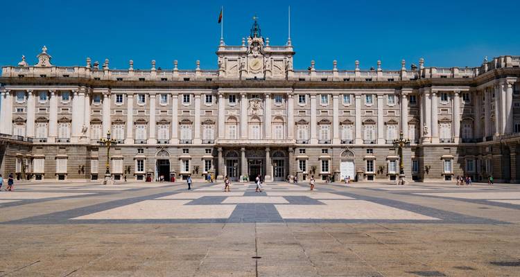 Grand Palais Royal de Madrid donnant sur une vaste place ouverte sous un ciel bleu dégagé.