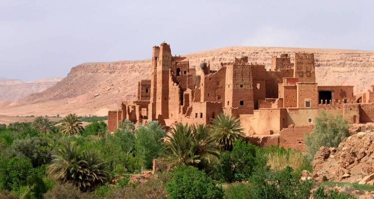 Ancienne kasbah en terre crue entourée de palmiers luxuriants avec des montagnes arides au-delà dans la vallée du Draa