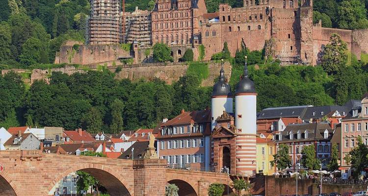 El pintoresco Castillo de Heidelberg se alza sobre el río Neckar y el histórico puente de piedra, con colinas boscosas de fondo.