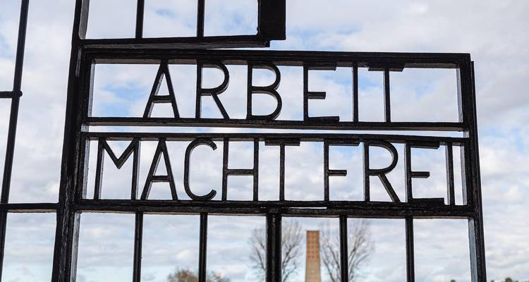 Inscription sur la porte en fer « Arbeit Macht Frei » à Sachsenhausen avec la tour commémorative floue en arrière-plan.