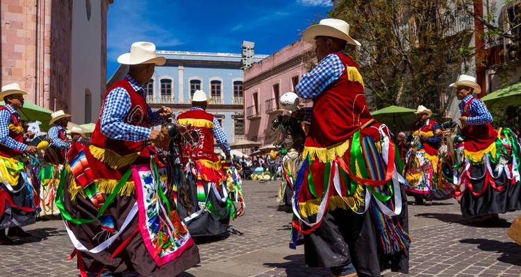 Bailarines con trajes coloridos, outfits con flecos y sombreros de vaquero actuando en una plaza de adoquines.