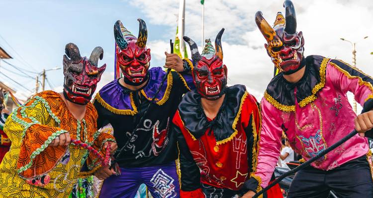 Cuatro performers con máscaras de diablo vividas y trajes bordados posando energéticamente para la cámara.