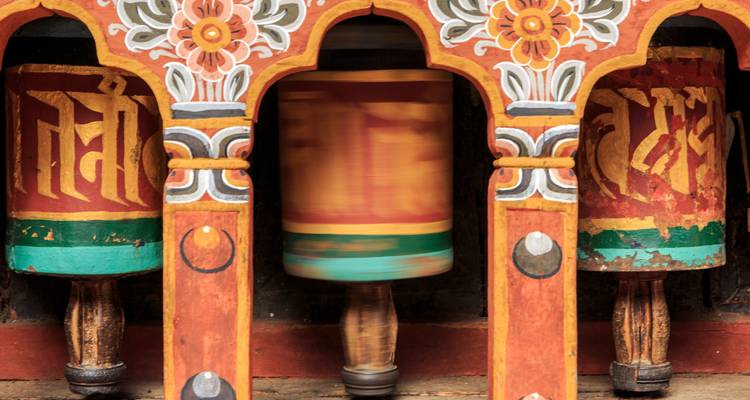 Primer plano de coloridas ruedas de oración de madera, una girando con desenfoque de movimiento dentro de un marco ornamentado.
