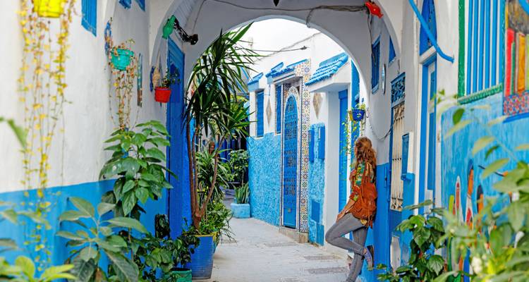 Callejón azul colorido con plantas y un viajero descansando, medina de Chefchaouen.
