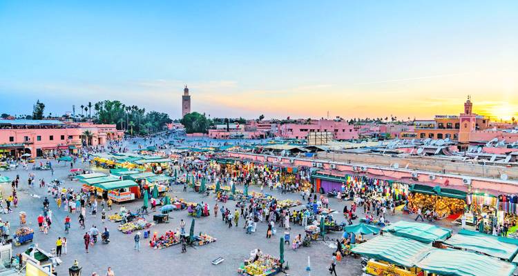 Vista nocturna sobre la animada Jemaa el-Fnaa mientras se pone el sol, con luces y multitudes llenando la histórica plaza.